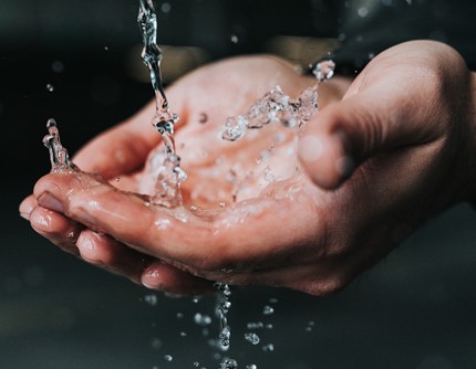 Person washing their hands under running water in a kitchen sink. 