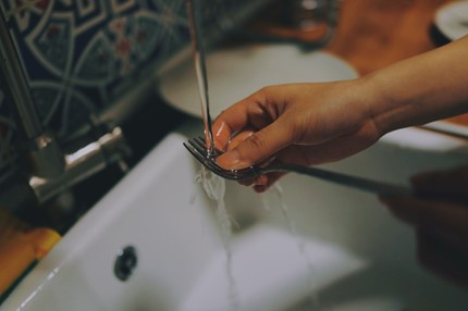A person washing a metal fork under a kitchen sink that is running water. 