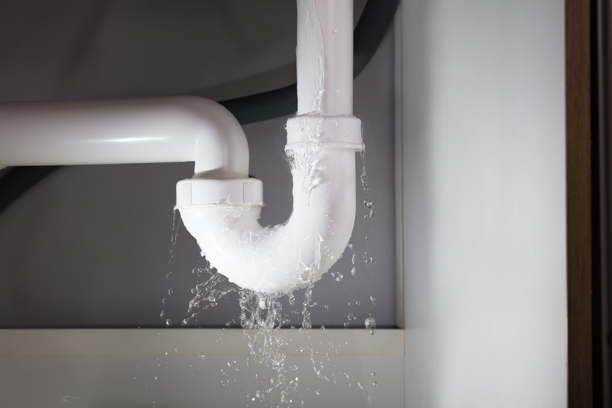 White pipes under a bathroom sink that is leaking large amounts of water from the bathroom sink. 
