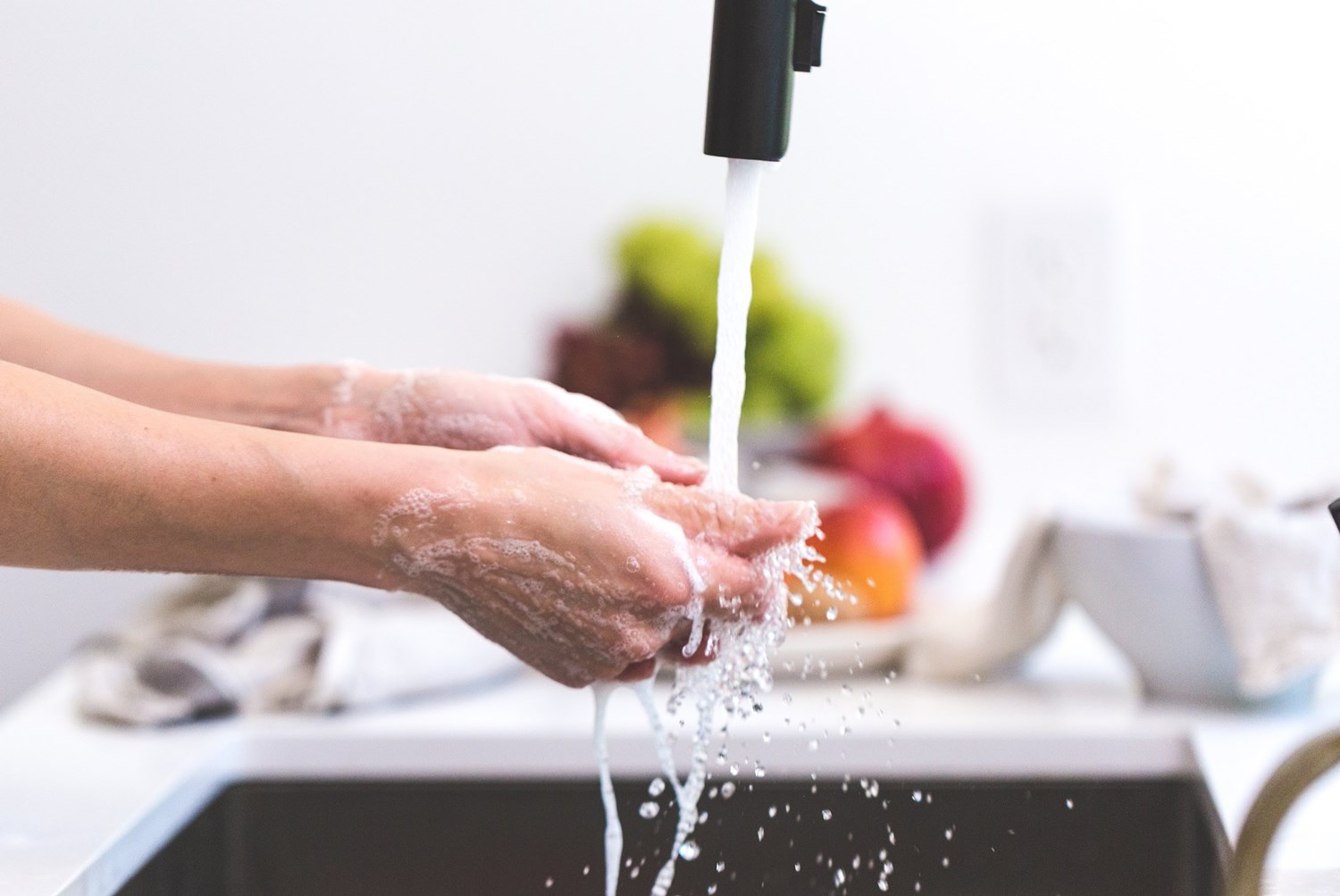 Woman washing her hands in her black kitchen sink with the water running. 