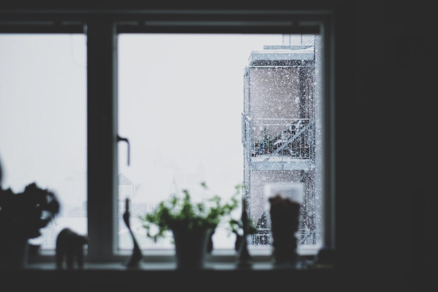Kitchen window that overlooks an apartment building that is covered with snow in the wintertime. 