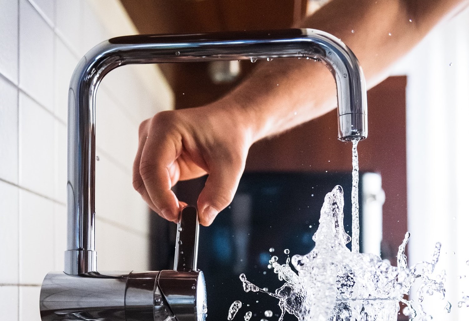 A woman turning of a gray kitchen sink that is running water in a clear glass. 