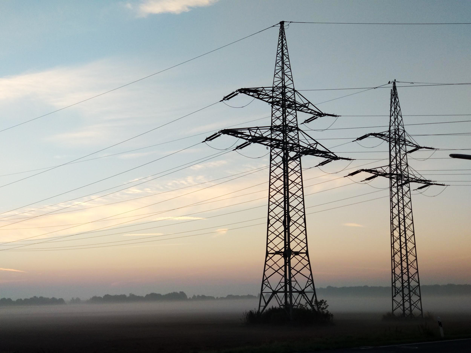 Two large electrical power lines with wires extending from the base based in a field. 