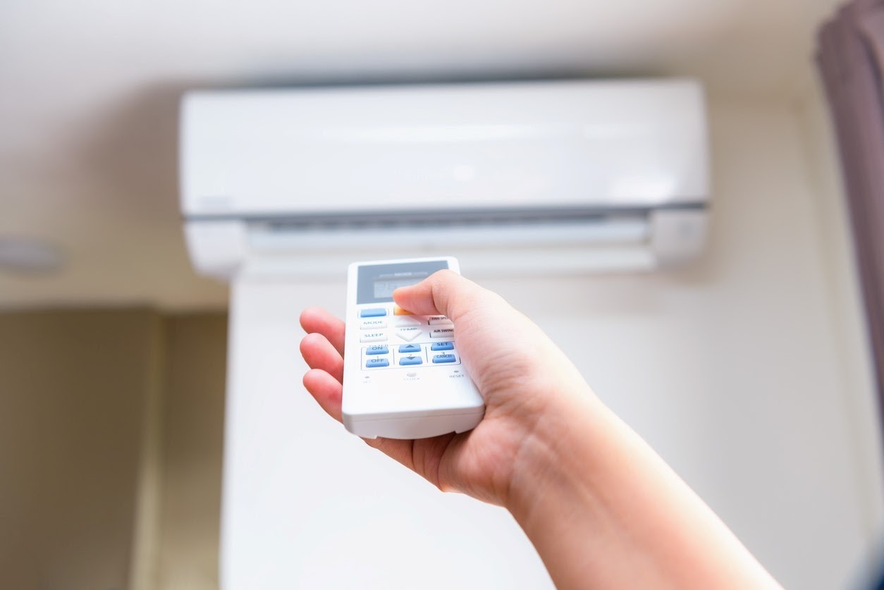 A homeowner attempting to turn on her AC unit by clicking the button on the white AC remote. 