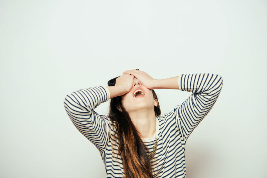 woman wearing a black and white striped shirt covering her eyes with her hands out of frustration. 