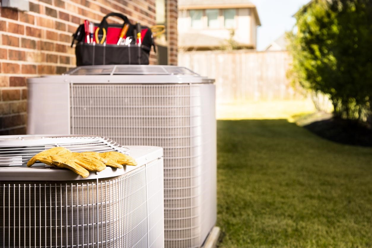 Two AC units outside of a D.C. region house with a CroppMetcalfe contractors tools and gloves resting next to the units. 