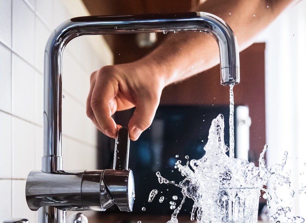 D.C. homeowner turning on the kitchen sink faucet to fill up a glass of water. 