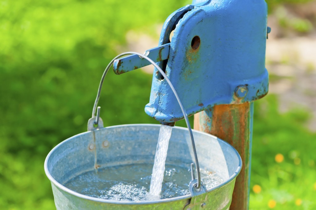 Private well system running water that is being poured into a metal bucket close to be full. 